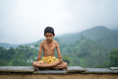 A young indian cute kid doing yoga in the mountains,wearing a dhoti