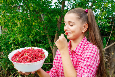 Girl holding berry fruits in bowl against plants