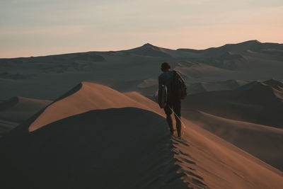 Rear view of man standing on land against sky during sunset