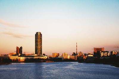 River by buildings against sky during sunset