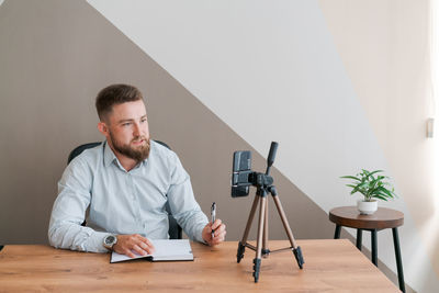 Young bearded businessman working in office sitting at table using smartphone