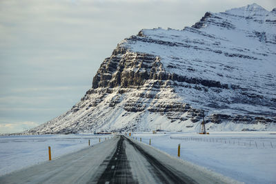 Snow covered road by mountain against sky