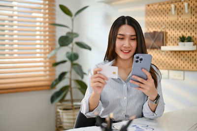 Portrait of young woman using mobile phone while sitting at home