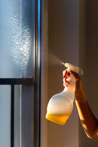 Close-up of hand holding bottle by window