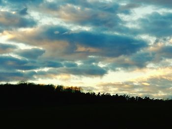 Silhouette trees on landscape against dramatic sky