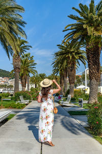 Rear view of young woman woman wearing summer style dress on promenade under palm trees
