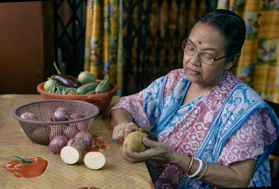 A simple looking aged bengali woman cutting vegetables inside her home