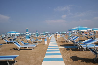 Deck chairs with parasols arranged on beach against sky during sunny day