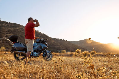 On the road.tourist man traveling on motorcycle, looking through binoculars at mountains in sunset
