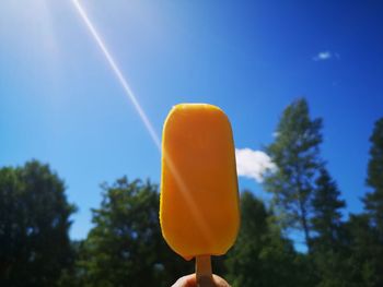 Close-up of hand holding ice cream against blue sky