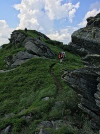 Low angle view of friends climbing on mountain against sky