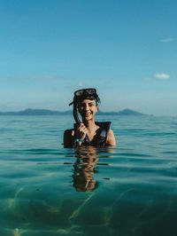 Portrait of young woman swimming in sea against blue sky