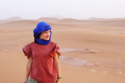 Portrait of smiling young woman standing in desert against sky