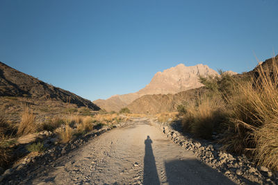 Road leading towards mountains against clear blue sky