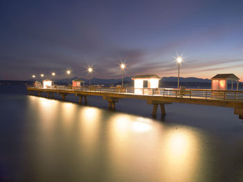 Illuminated bridge over river against sky at night