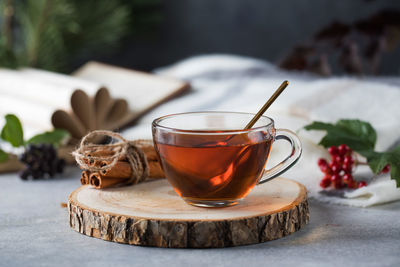 A glass cup of tea with a golden spoon and a book on a gray table