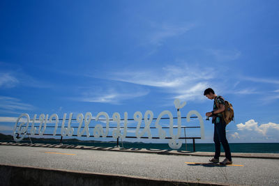 Side view of man standing by text against blue sky