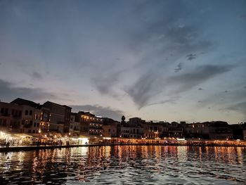 River by illuminated buildings against sky at sunset