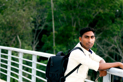 Portrait of young man on railing against trees