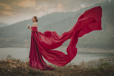 Woman in red dress standing at lakeshore during sunset