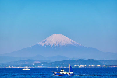 Scenic view of sea and snowcapped mountain against clear blue sky