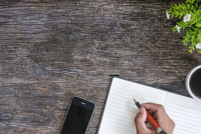 Directly above shot of person writing in book by plant and mobile phone on table