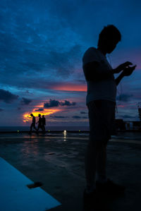 Silhouette people standing by sea against sky at sunset