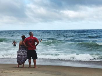 Rear view of man and woman at beach against sky