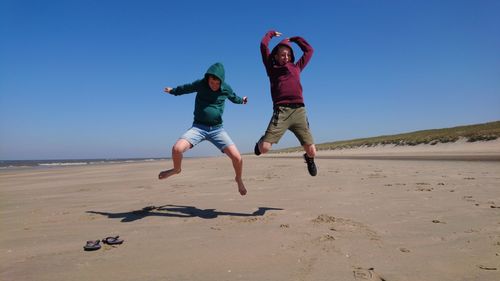 Full length of man jumping on sand against clear sky