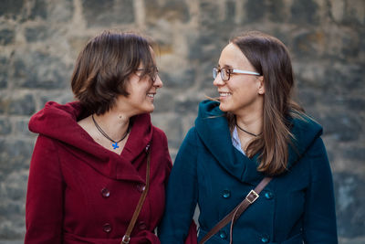 Smiling sisters standing against stone wall