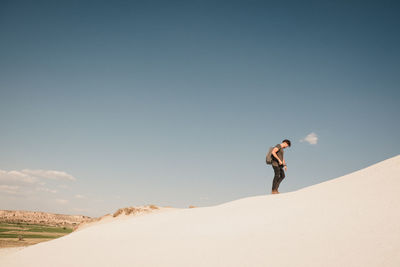 Young man walking in desert against sky