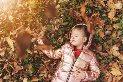 Happy little blonde girl laying on yellow autumn leaves in garden. child smiles and has fun in park