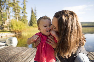 Mother kissing cheerful son on pier against lake