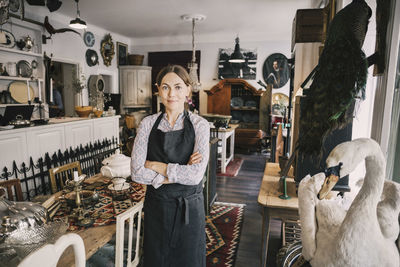 Portrait of female retailer with arms crossed standing in antique shop