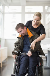 Female caretaker assisting disabled man on wheelchair at home