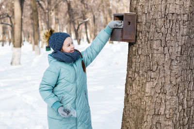 A girl puts seeds in a bird feeder on a tree in a winter park. animal care.
