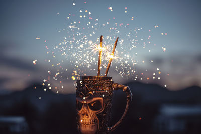 Close-up of sparklers in mug against sky