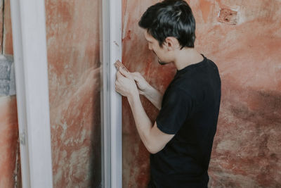One caucasian young man cleans a window frame with a construction knife 