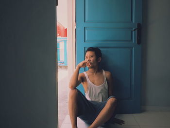 Young woman looking away while sitting on door of home