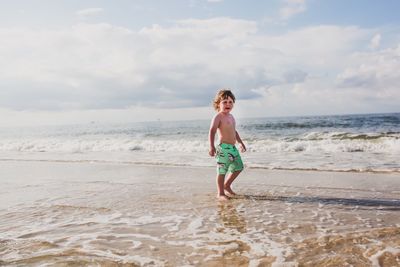 Boy walking on sand at beach against sky