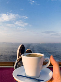 Coffee cup on table by sea against sky