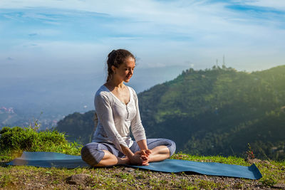 Side view of young woman sitting on mountain