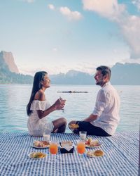 Couple having food and drinks while sitting by sea