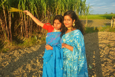 Portrait of friends holding crop standing at farm