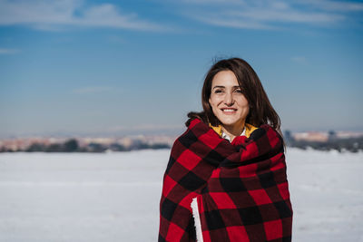 Smiling young woman standing in snow against sky