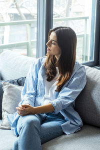 Young woman using phone while sitting on sofa at home