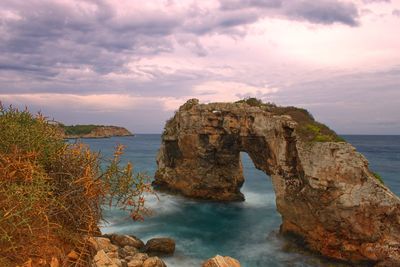 Rock formation in sea against sky during sunset