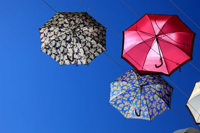 Low angle view of umbrellas hanging on cable against clear blue sky