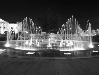 Fountain in city against sky at night