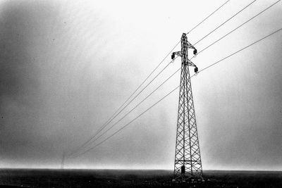 Electricity pylon by sea against clear sky